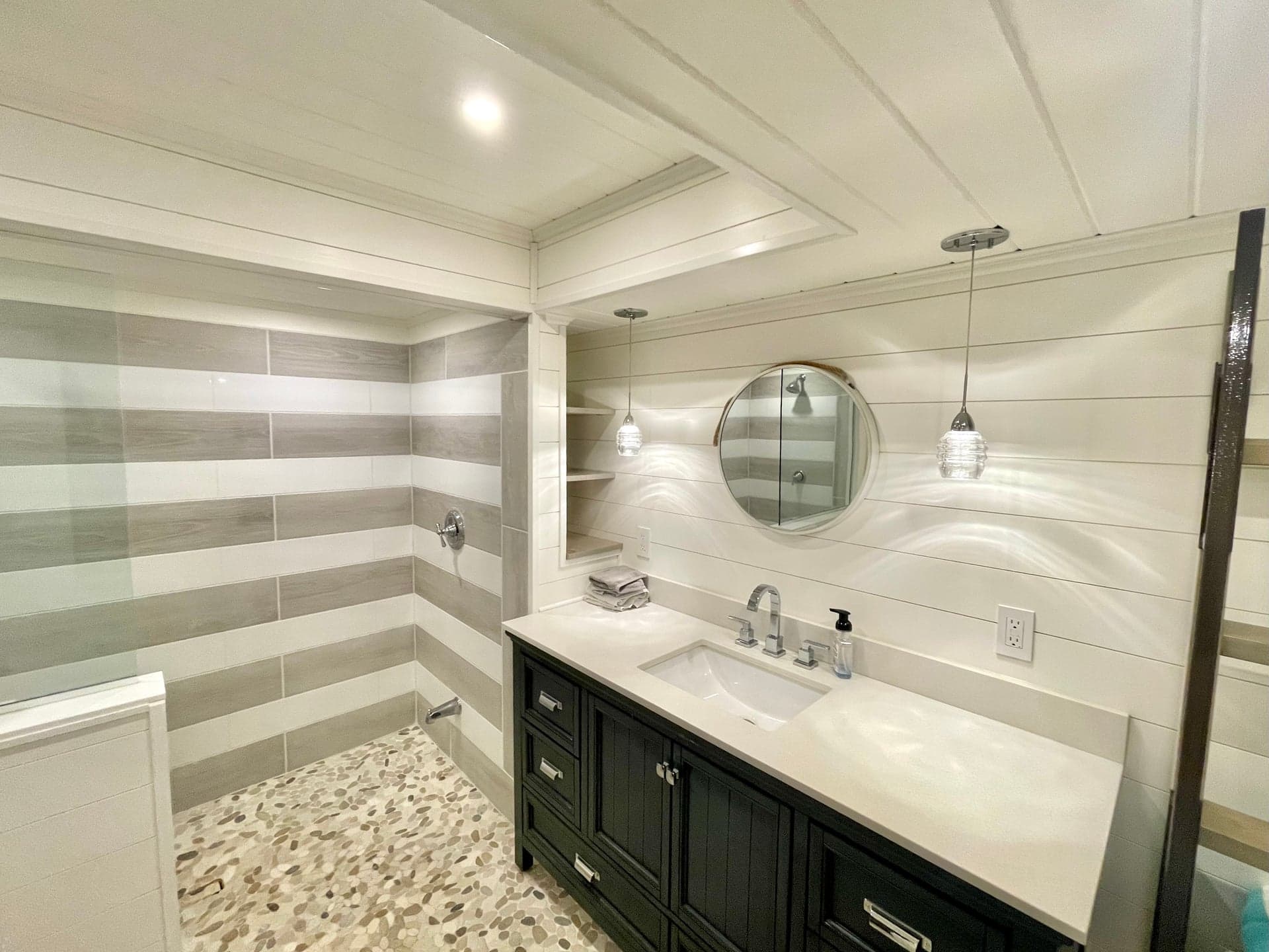 Bathroom with striped wall tile, pebble mosaic floor, and dark vanity